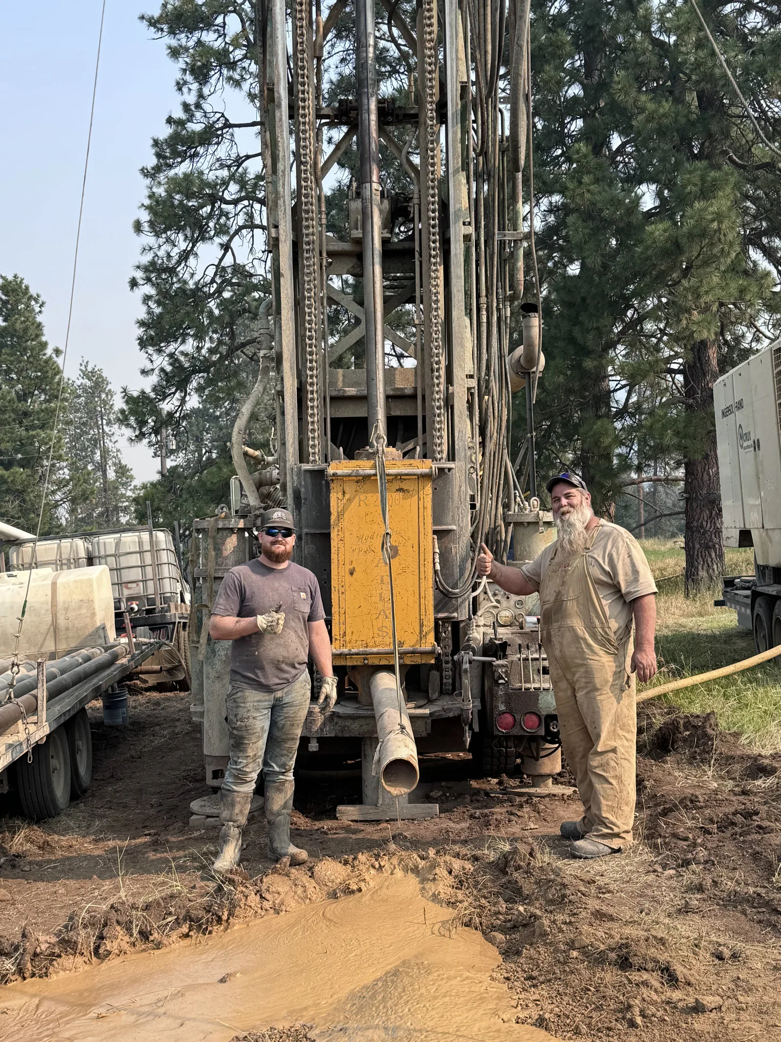 Pike and Jay Langer standing in front of their drill rig on a job site near Midvale, Idaho